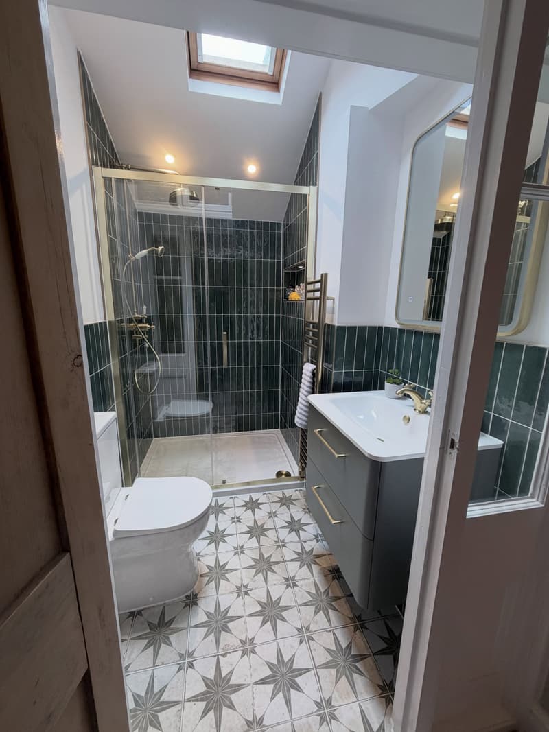 En-suite shower room with green metro tiles, brass fittings, patterned floor tiles and skylight