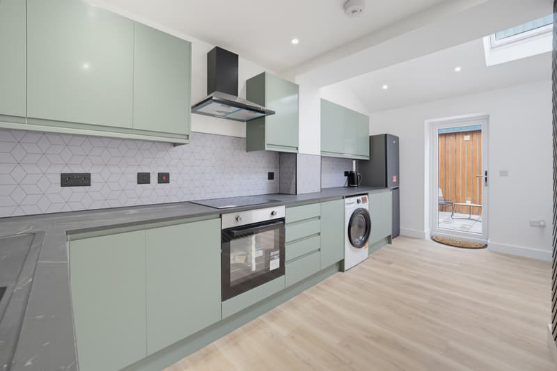 Sage green shaker-style kitchen with built-in oven and laundry space in a Cardiff flat