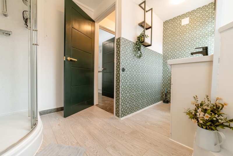 Bathroom with green tiles, black vanity, round mirror and plants